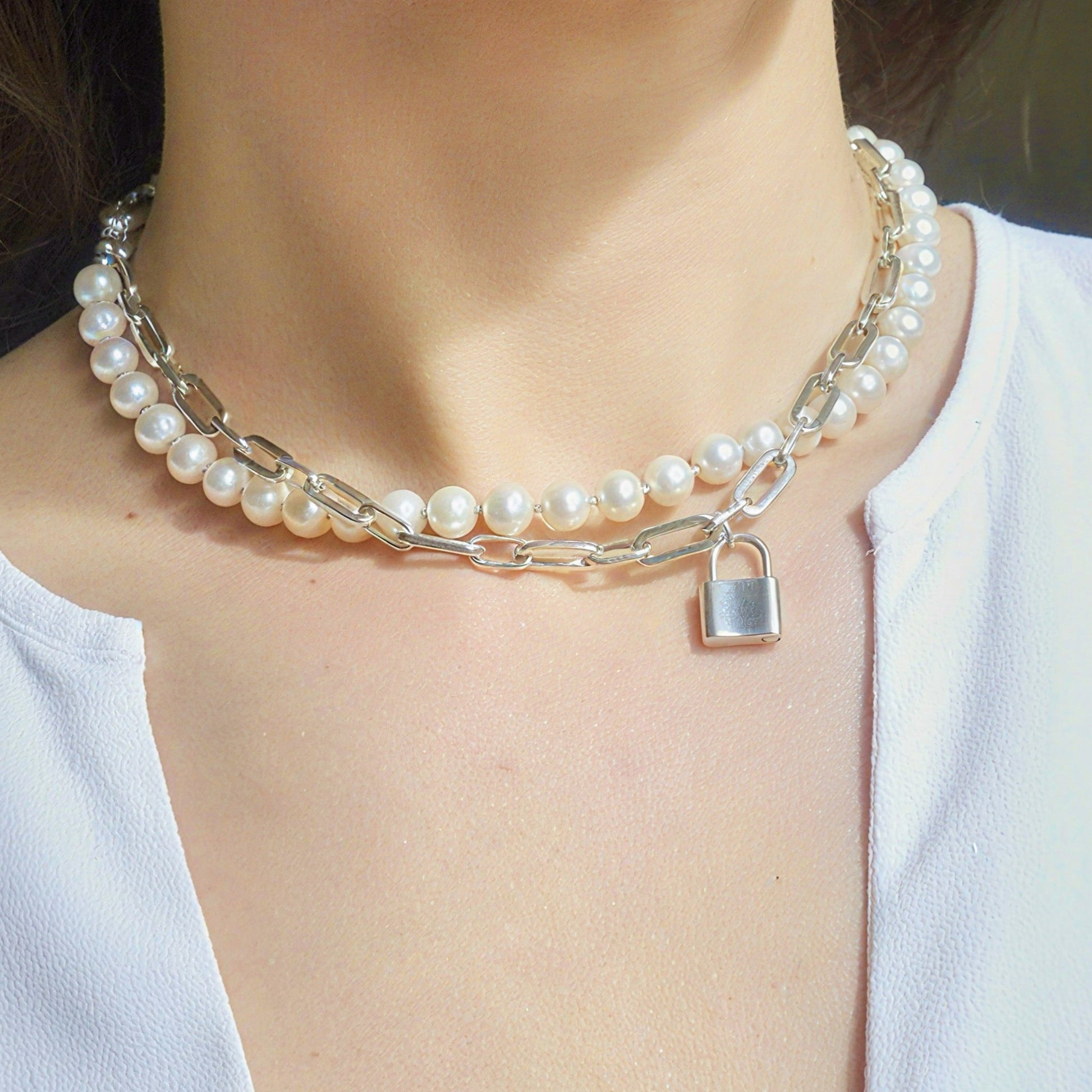Pearl necklace with a silver lock charm on a person wearing a white top.