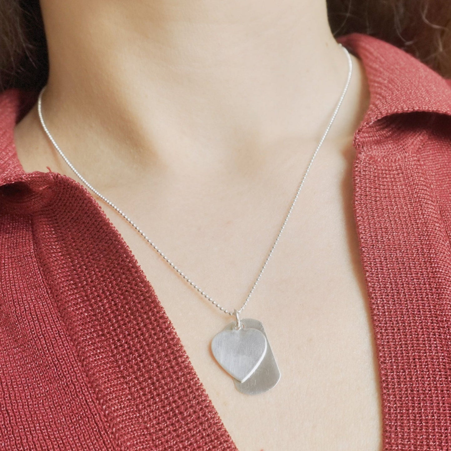 Person wearing a silver necklace with a heart-shaped pendant against a red garment.