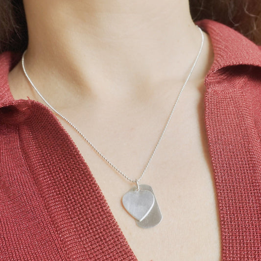 Person wearing a silver necklace with a heart-shaped pendant against a red garment.