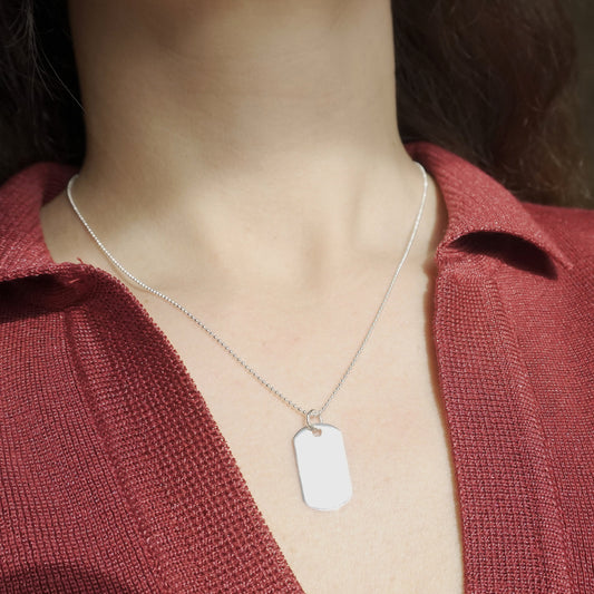 Person wearing a silver necklace with a dog tag against a blurred background
