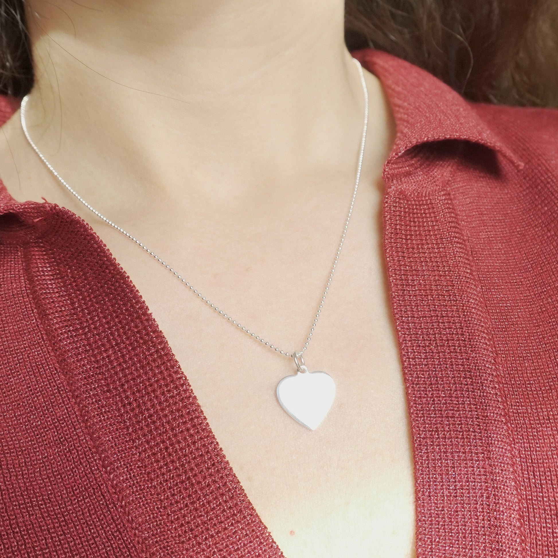 Person wearing a silver necklace with a heart-shaped pendant against a blurred background